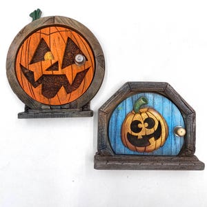 May include: Two Halloween-themed decorative door plaques. One is round, the other is a pentagon shape. Both have a wooden frame and a carved pumpkin face. The round plaque is orange and brown, while the other has a blue background.