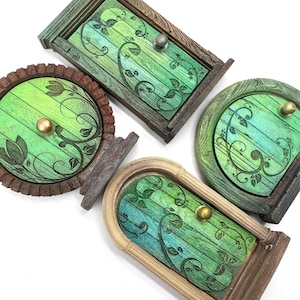 May include: Four miniature wooden doors in various shapes, each with a green and blue painted finish and decorative leaf patterns. The doors have different frame styles, including a round, rectangular, and arched design, with metallic knobs.