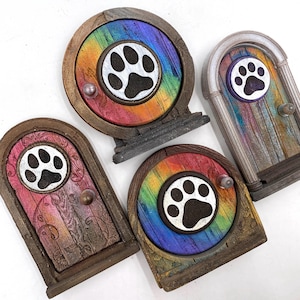 Op de afbeelding: Een verzameling decoratieve elfendeuren met een pootafdrukontwerp. De deuren hebben een regenboogkleurenschema en een houten frame. Elke deur heeft een kleine knop en een pootafdruk in het midden.