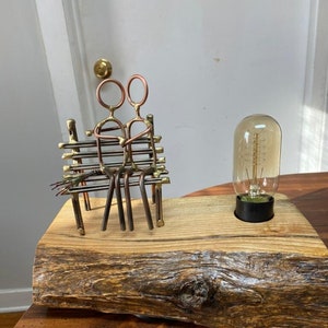 May include: A rustic wooden lamp base with a metal sculpture of a couple sitting on a bench. The lamp has a clear glass bulb with a filament.