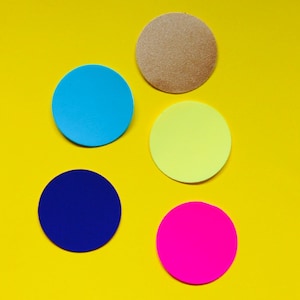 May include: Five colorful, circular objects on a yellow background. The circles are blue, brown, yellow, dark blue, and pink. The brown circle has a textured surface. The objects are arranged in a scattered pattern.