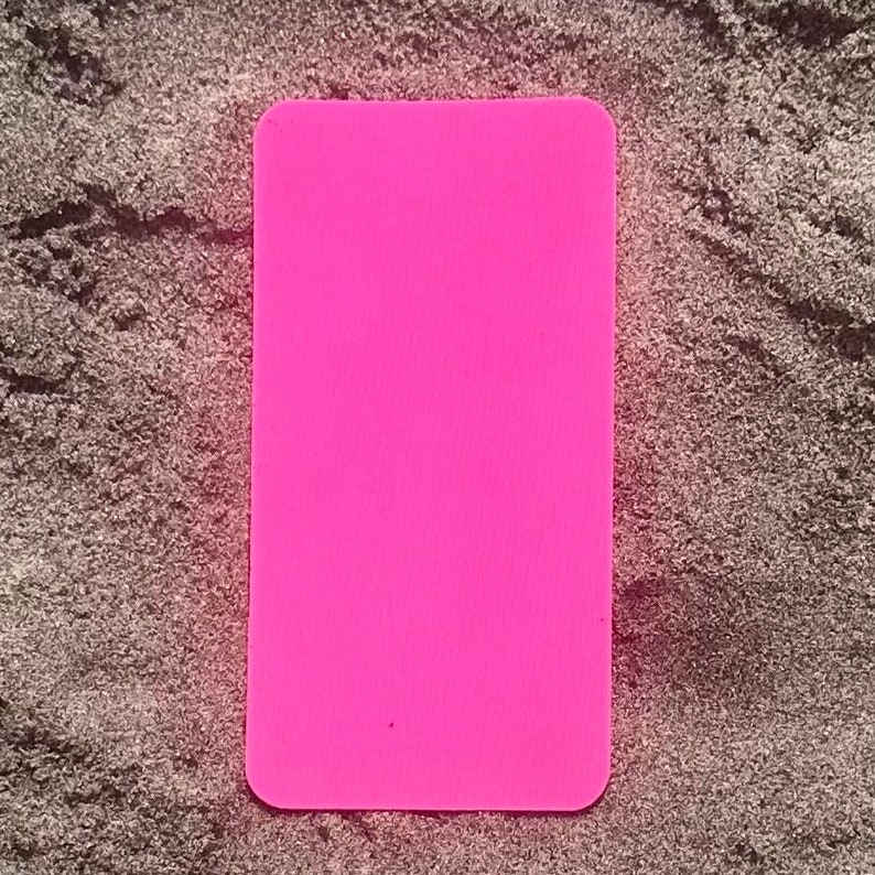 Op de afbeelding: Een helder, magenta rechthoekig object met afgeronde hoeken. Het is geplaatst tegen een getextureerde, grijze achtergrond. Het gladde oppervlak van de magenta rechthoek contrasteert met de ruwe achtergrond.