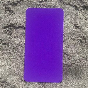 Op de afbeelding: Een effen paarse rechthoekige kaart met afgeronde hoeken. De kaart heeft een levendige paarse tint en een getextureerd oppervlak. De kaart ligt op een grijs, getextureerd oppervlak.