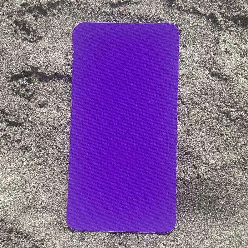 Op de afbeelding: Een effen paarse rechthoekige kaart met afgeronde hoeken. De kaart heeft een levendige paarse tint en een getextureerd oppervlak. De kaart ligt op een grijs, getextureerd oppervlak.