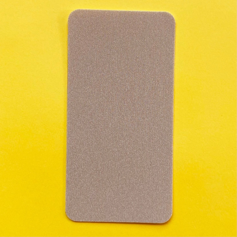 Op de afbeelding: Een rechthoekige, beige stoffen patch met afgeronde hoeken. De patch heeft een getextureerd, geribbeld oppervlak en staat tegen een heldergele achtergrond.