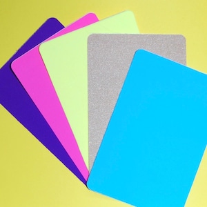May include: Five different colored sheets of paper arranged in a fan shape. The colors are purple, pink, light green, gray, and light blue.