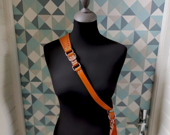 May include: A brown leather camera strap with silver hardware and stitching. The strap is worn over a black mannequin.