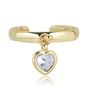 May include: A gold-colored ring with a heart-shaped pendant. The pendant features a clear, faceted stone set within a gold frame. The ring has a smooth, polished finish and a simple, elegant design.