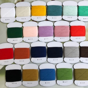 Op de afbeelding: Een verzameling van 28 spoelen garen, elk gewikkeld met een andere kleur garen. De spoelen zijn gerangschikt in rijen en gelabeld met nummers van 201 tot 228.