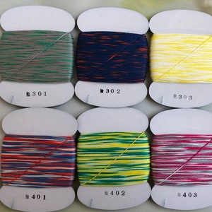 May include: Six spools of colorful thread, each with a different color combination. The threads are wound on white cardboard spools, with the numbers 301, 302, 303, 401, 402, and 403 printed on the front. The threads are various colors, including green, blue, yellow, and red.