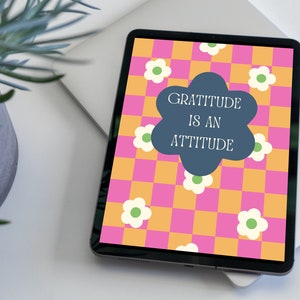 Peut inclure: Une tablette numérique affiche un motif floral coloré avec le texte "GRATITUDE IS AN ATTITUDE". L'arrière-plan présente un motif à carreaux rose et orange avec des fleurs blanches et vertes.