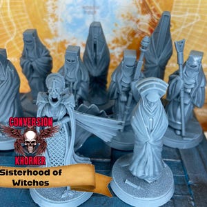Puede incluir: Un conjunto de figuras en miniatura grises, posiblemente para juegos de mesa, que representan figuras con túnicas y un personaje central con rostro esquelético. Las figuras están sobre una superficie azul, con una pancarta "Sisterhood of Witches".
