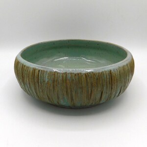 May include: A round ceramic bowl featuring a smooth, light mint green interior with subtle dark speckles. The exterior has a textured, vertical ribbed pattern in a warm brown tone, with the mint green glaze dripping over the top rim edge.