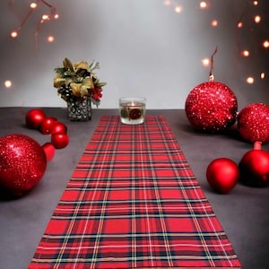 May include: Red and black tartan table runner with red Christmas baubles and a candle on a table.