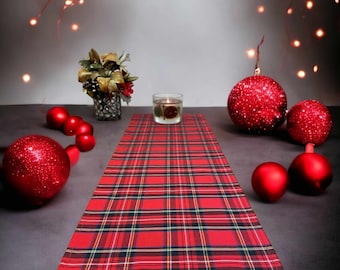 May include: Red and black plaid table runner with red Christmas ornaments and a candle on a table.