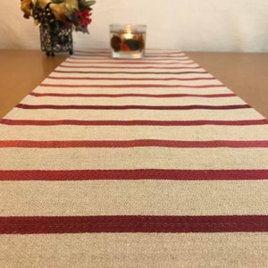 Puede incluir: Un camino de mesa a rayas beige y burdeos con una vela en un tarro de vidrio encima.