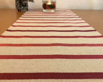 May include: A beige and burgundy striped table runner with a candle in a glass jar on top of it.