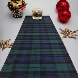 May include: A green and blue plaid table runner with a candle in a clear glass jar on top of it.
