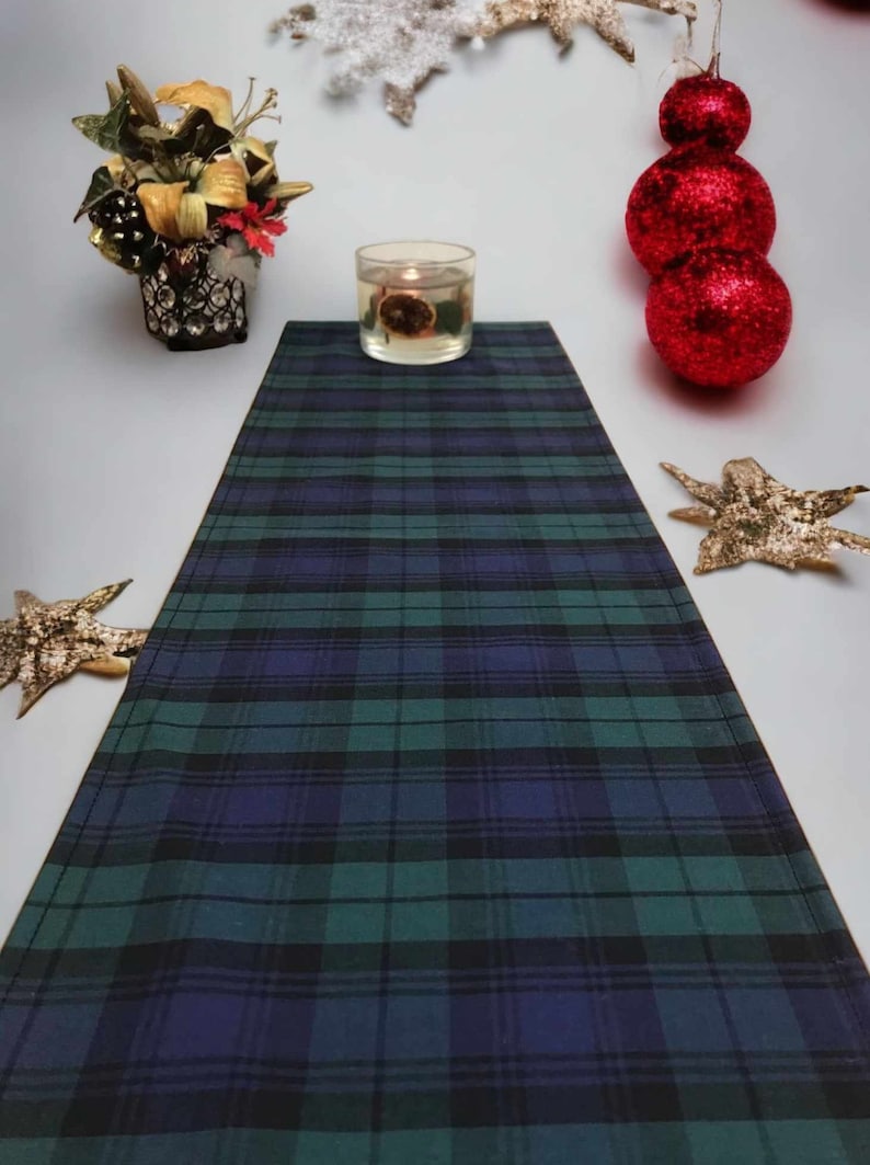 May include: A green and blue plaid table runner with a candle in a clear glass jar on top of it.