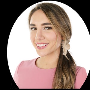 Puede incluir: Una mujer con el pelo largo y casta&ntilde;o claro lleva un vestido rosa y pendientes grandes de color beige. Est&aacute; sonriendo y mirando a la c&aacute;mara.