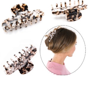 Puede incluir: Una pinza para el cabello con un patr&oacute;n de carey en colores moteados negro, marr&oacute;n y blanco. La pinza tiene una serie de dientes entrelazados y un mecanismo de bisagra con resorte. El dise&ntilde;o se muestra desde varios &aacute;ngulos y en uso.