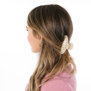 Puede incluir: Una mujer con el pelo largo y casta&ntilde;o lleva una camisa rosa y una gran pinza para el pelo de color beige tejida.