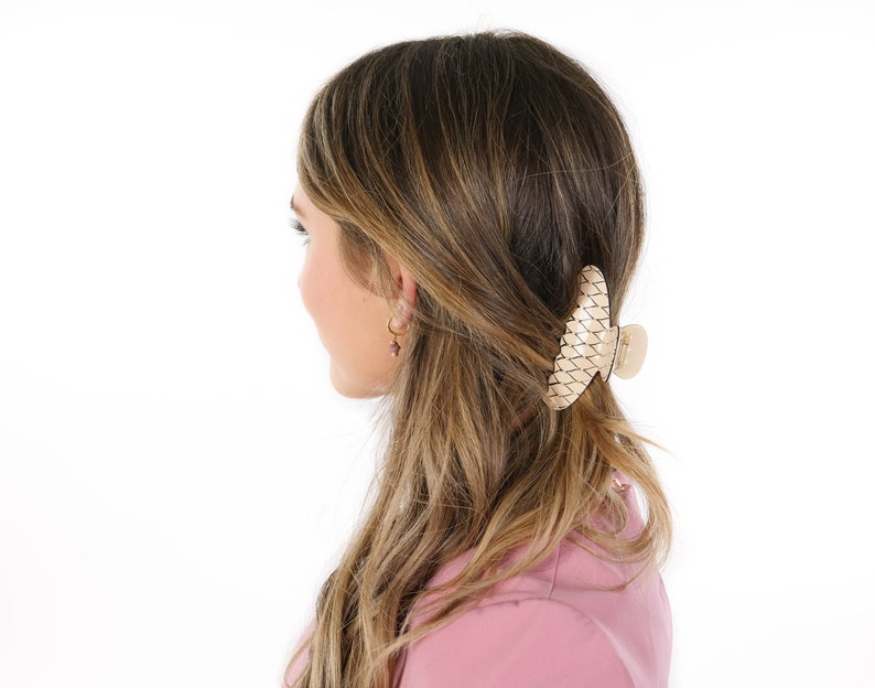 Puede incluir: Una mujer con el pelo largo y casta&ntilde;o lleva una camisa rosa y una gran pinza para el pelo de color beige tejida.