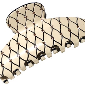 Puede incluir: Una gran pinza para el pelo de color marfil con un patr&oacute;n geom&eacute;trico negro y dorado. La pinza est&aacute; decorada con peque&ntilde;os diamantes de imitaci&oacute;n transparentes.