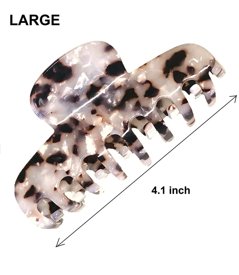 Puede incluir: Una pinza de pelo grande con un patr&oacute;n de carey blanco y negro. La pinza presenta una serie de dientes entrelazados y est&aacute; etiquetada como LARGE con una medida de 10,4 cm indicada por una flecha de doble punta en la imagen.