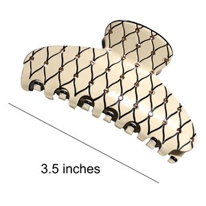 Puede incluir: Una gran pinza para el pelo de pl&aacute;stico de color blanco roto con un patr&oacute;n geom&eacute;trico negro y dorado. La pinza mide 3,5 pulgadas de largo.