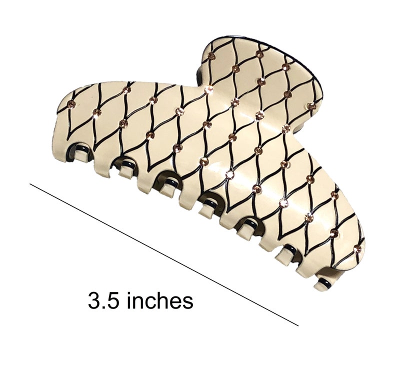 Puede incluir: Una gran pinza para el pelo de pl&aacute;stico de color blanco roto con un patr&oacute;n geom&eacute;trico negro y dorado. La pinza mide 3,5 pulgadas de largo.