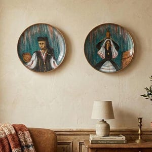May include: Two circular decorative wall plates featuring detailed illustrations of figures in traditional attire. The left plate depicts a person in a dark cap and vest, while the right plate shows a person holding a vessel above their head.