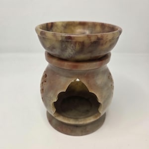Peut inclure: Un brûleur d'huile en pierre sculptée avec un dessus en forme de bol et une base décorative. Le chauffe-huile est principalement beige et marron avec des motifs floraux sculptés et une grande ouverture arquée. Le design est symétrique.