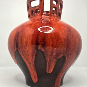 May include: A ceramic vase featuring a glossy, vibrant orange glaze that drips down over a dark brown base. The neck of the vase is designed with a distinctive open-work, grid-like lattice structure, creating a unique silhouette for this piece.