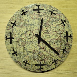 May include: A round clock with a map-like design featuring black airplane silhouettes around the clock face. The clock hands are black and point to the 12 and 4 o'clock positions.