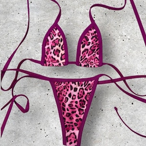 May include: A two-piece bikini set featuring a pink leopard print design with dark pink trim. The top is a triangle style, and the bottom is a thong style. The bikini has thin, adjustable straps.