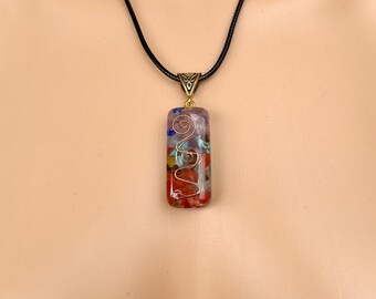 May include: A rectangular pendant necklace with a black cord. The pendant is made of clear resin with embedded colorful stones and a gold wire design.