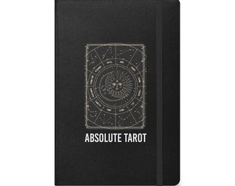 Può includere: Quaderno nero con un disegno di carta dei tarocchi color oro con simboli zodiacali, un sole e una luna crescente. Il testo "ABSOLUTE TAROT" è stampato in bianco. Un elastico nero assicura il quaderno.