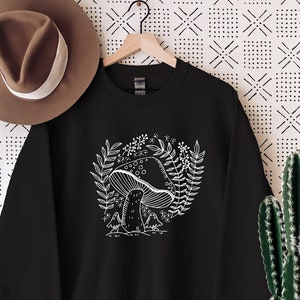 Puede incluir: Sudadera negra con un gr&aacute;fico blanco de un hongo con hojas y flores.