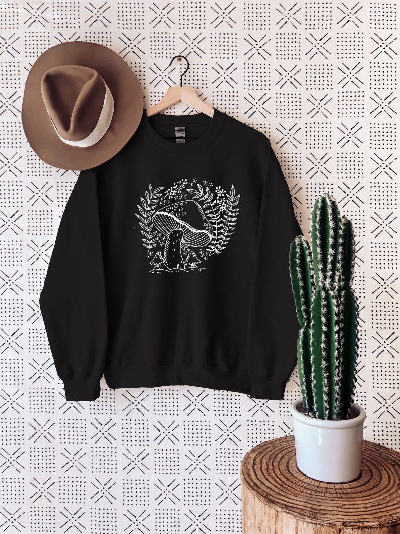 Puede incluir: Sudadera negra con un gr&aacute;fico blanco de un hongo con hojas y flores.