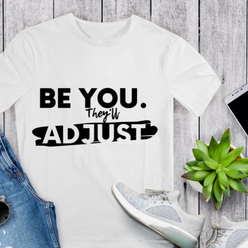 May include: White t-shirt with black text that reads "BE YOU. They'll ADJUST".