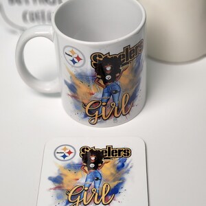 May include: White ceramic mug with a black and yellow Steelers logo and a cartoon image of a woman wearing a black jersey, blue jeans, and a black face mask. The mug has the words "Steelers Girl" in gold lettering. A matching coaster with the same design is also shown.