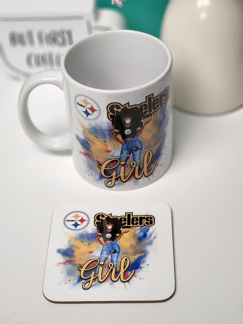 May include: White ceramic mug with a black and yellow Steelers logo and a cartoon image of a woman wearing a black jersey, blue jeans, and a black face mask. The mug has the words "Steelers Girl" in gold lettering. A matching coaster with the same design is also shown.