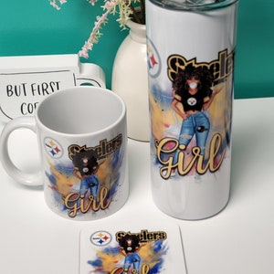 May include: A set of three Steelers-themed items: a mug, a tumbler, and a coaster. Each item features a black woman with an afro wearing a Steelers jersey and jeans, with the words "Steelers Girl" in yellow and black lettering. The background is a watercolor-style design with yellow, blue, and black colors.