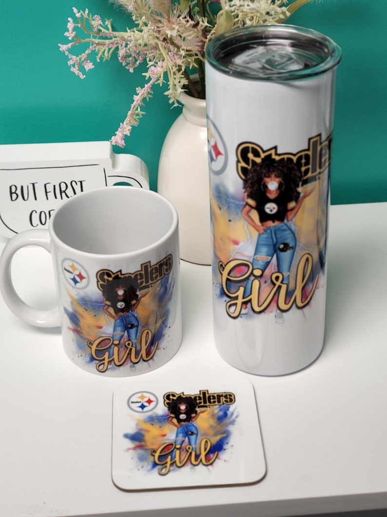 May include: A set of three Steelers-themed items: a mug, a tumbler, and a coaster. Each item features a black woman with an afro wearing a Steelers jersey and jeans, with the words "Steelers Girl" in yellow and black lettering. The background is a watercolor-style design with yellow, blue, and black colors.