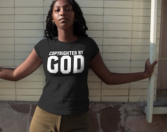 May include: Black t-shirt with the text "COPYRIGHTED BY GOD" in white block letters. The shirt has a crew neck and short sleeves. The person is wearing olive green pants.