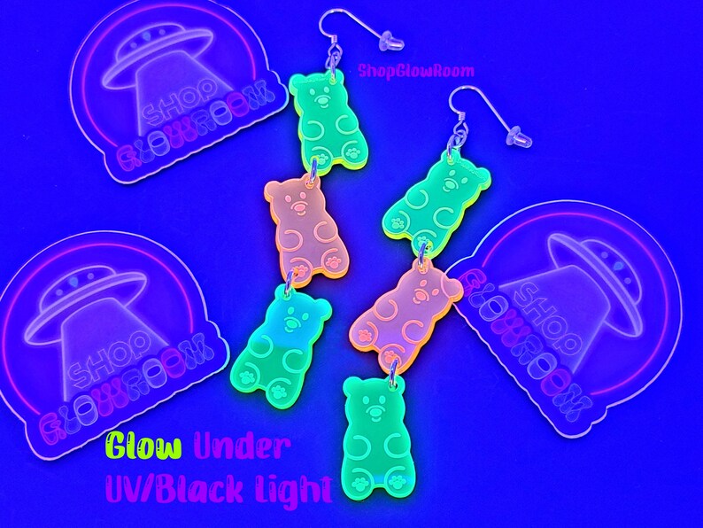 May include: Five pairs of glow-in-the-dark gummy bear earrings. The earrings are made of clear acrylic and feature a gummy bear design. The earrings are available in a variety of colors, including pink, green, yellow, and orange. The earrings are shown against a blue background. ShopGlowRoom.