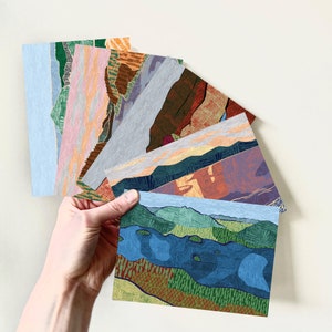 May include: A set of eight illustrated postcards featuring various landscape scenes. The postcards are printed on a textured paper stock and feature a variety of colours, including blue, green, brown, and orange.