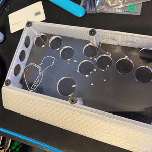 May include: A clear acrylic box with a white textured base. The box has 10 circular openings and a graphic of a taco with a bite taken out of it.