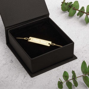 May include: A gold bar bracelet with the inscription "Only You" in a black velvet box.
